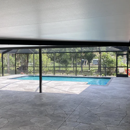 An insulated panel roof for a patio leading to a screen enclosure surrounding a backyard pool.